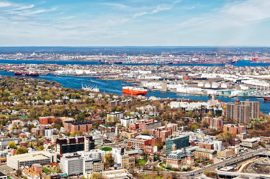 Aerial view of a city with residential neighborhoods in the foreground and a river port with cargo ships in the background
