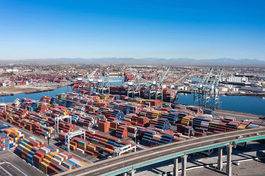 Busy container port with cargo cranes, stacked shipping containers, and harbor waters.