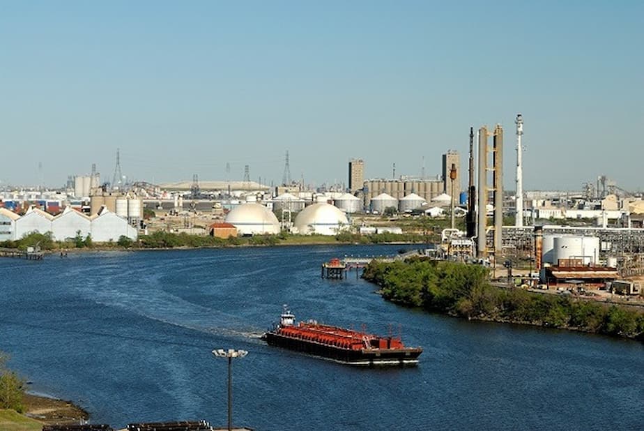 Industrial waterfront with storage tanks, refinery towers, and a barge on a river
