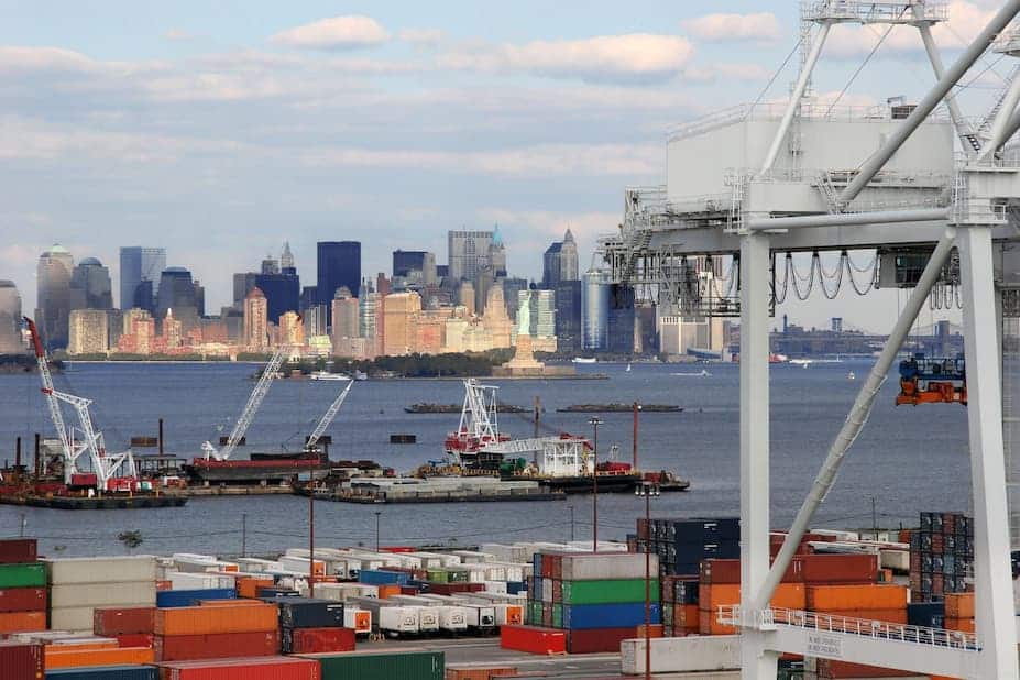 Shipping containers and port cranes with a city skyline across the harbor