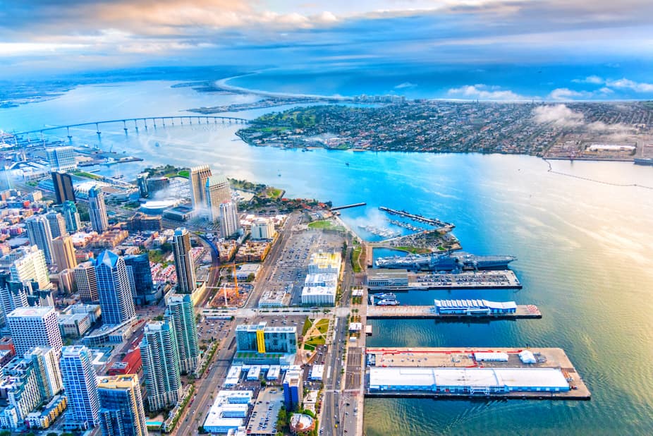 Aerial view of a waterfront city with downtown high-rises, piers, and a long bridge spanning the bay