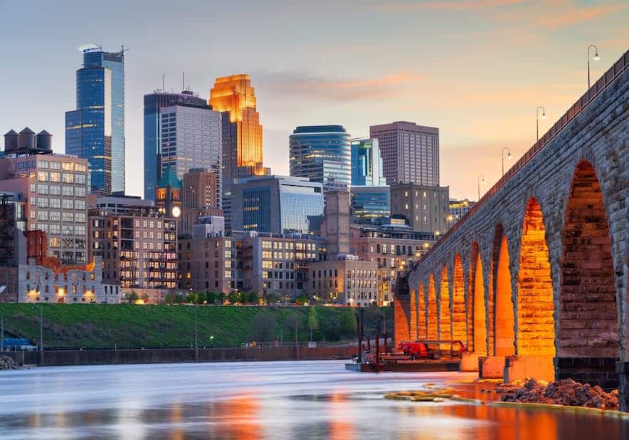 Minneapolis-St. Paul skyline at dusk with illuminated stone arch bridge reflected on the river